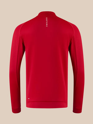 A red long-sleeve athletic quarter-zip pullover shown from the back, featuring a vertical white 'CASTORE' logo on the upper back, set against a solid beige background.