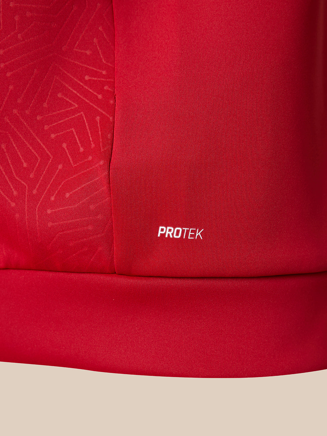 Close-up of a red athletic garment showing a seam with a subtle circuit-like texture on one side and a small white PROTEK logo on the fabric.