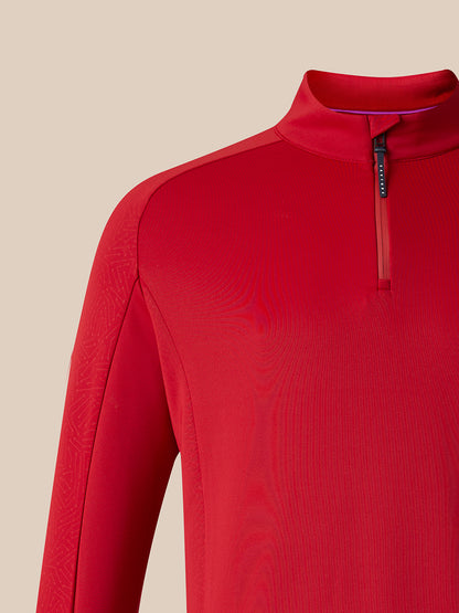 A close-up of a red long-sleeve athletic quarter-zip pullover, showing the collar, zipper, and textured fabric against a solid beige background.
