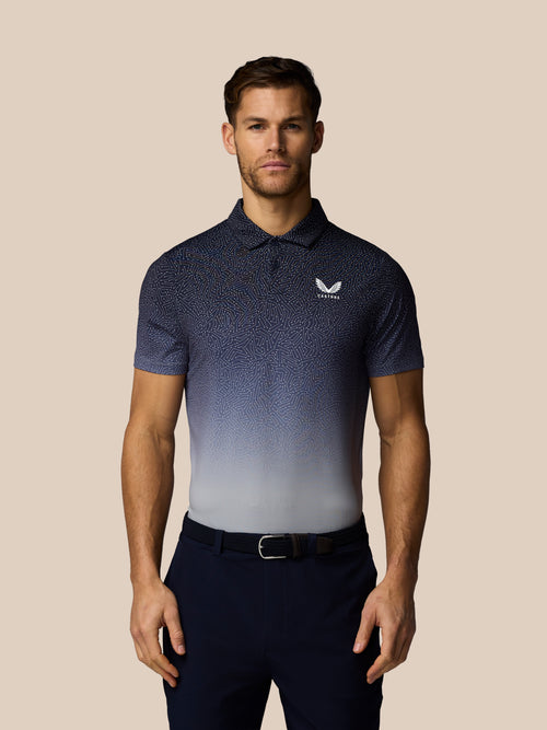 Man wearing a navy blue patterned polo shirt with a logo on a beige background