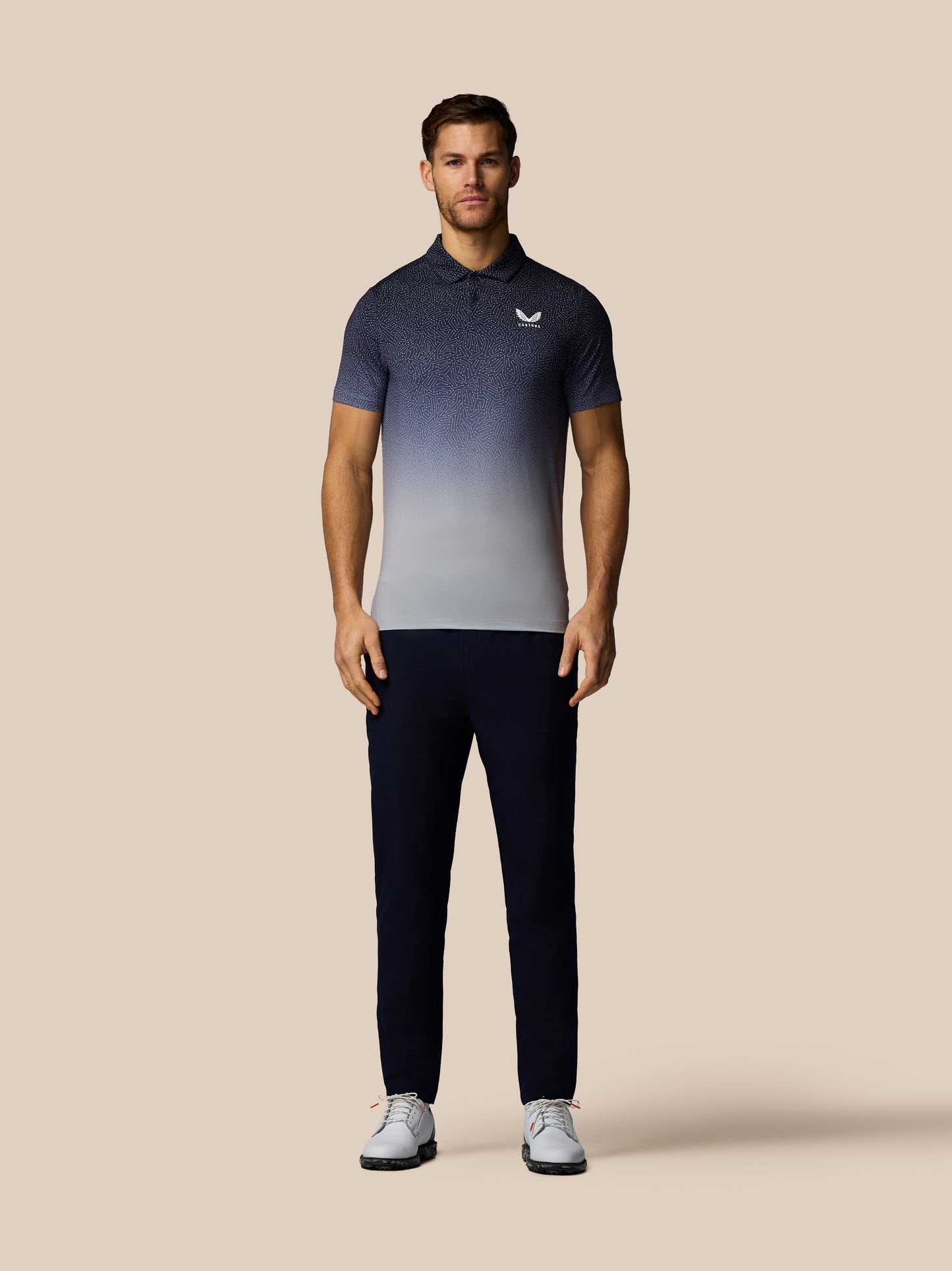 Man wearing a gradient polo shirt and dark pants on a beige background