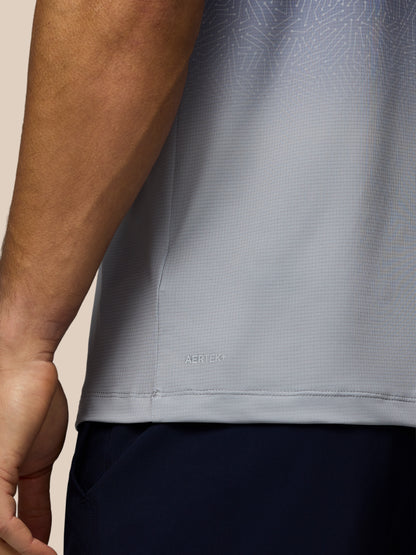 Close-up of a person wearing a light gray textured athletic shirt with a subtle geometric pattern and dark navy shorts against a plain beige background.