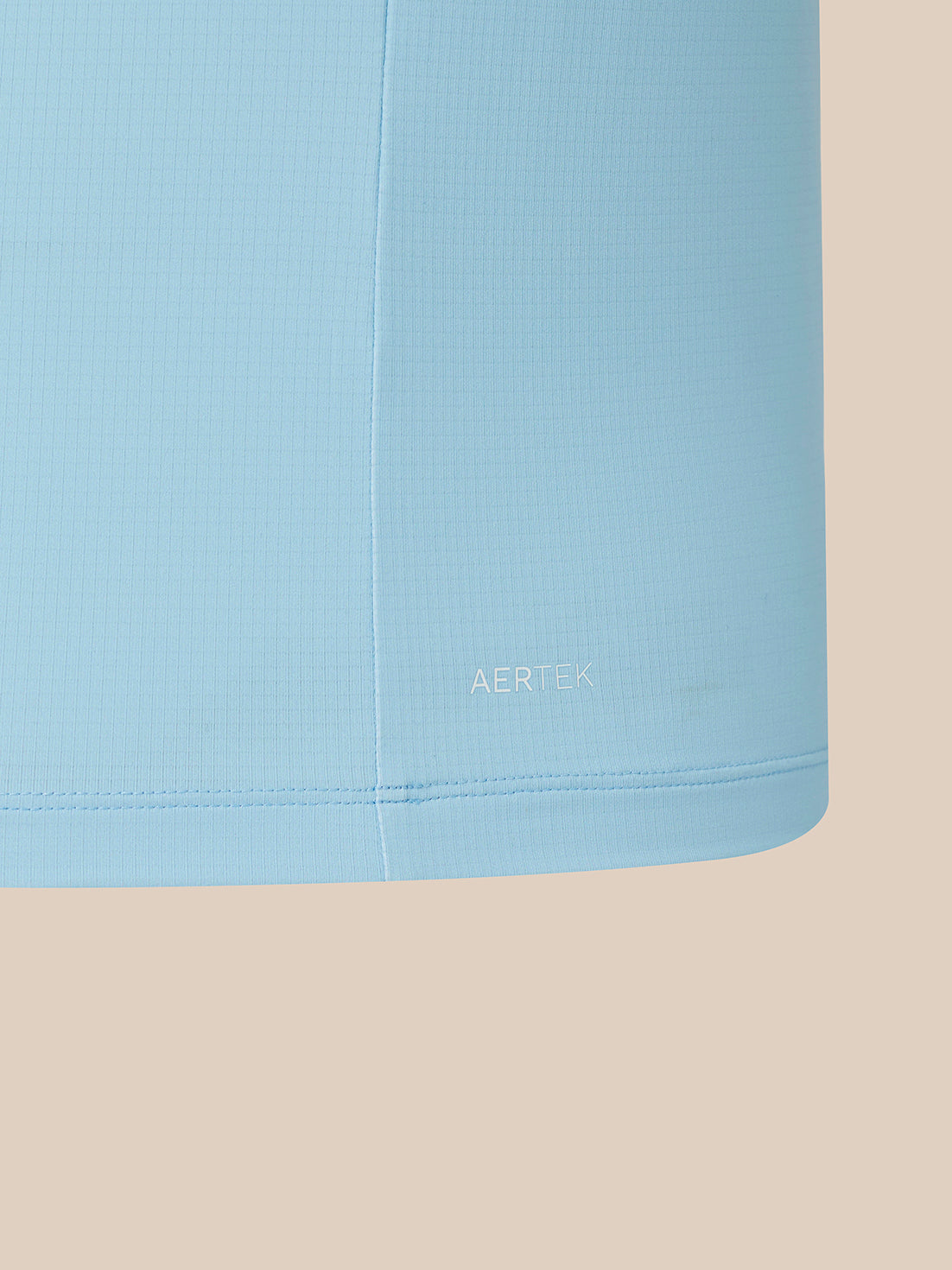A close-up of a light blue athletic fabric panel with a fine grid texture, featuring the AERTEK logo printed in white near the bottom hem, set against a solid beige background.