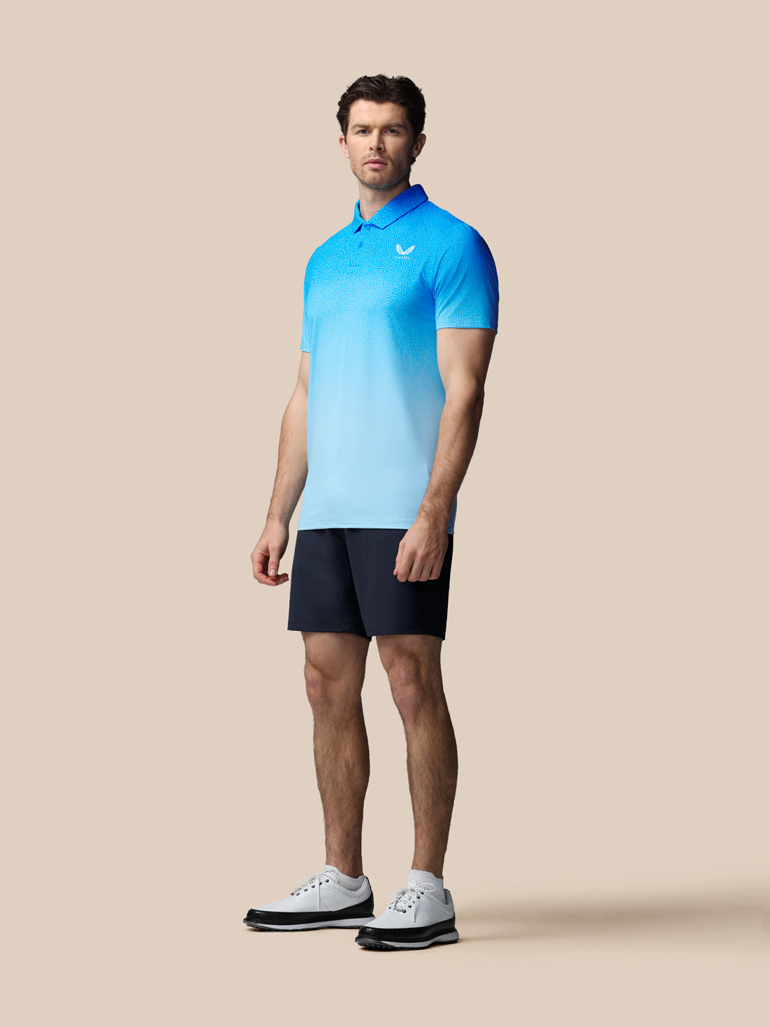 Man wearing a blue Castore polo shirt and black shorts on a beige background