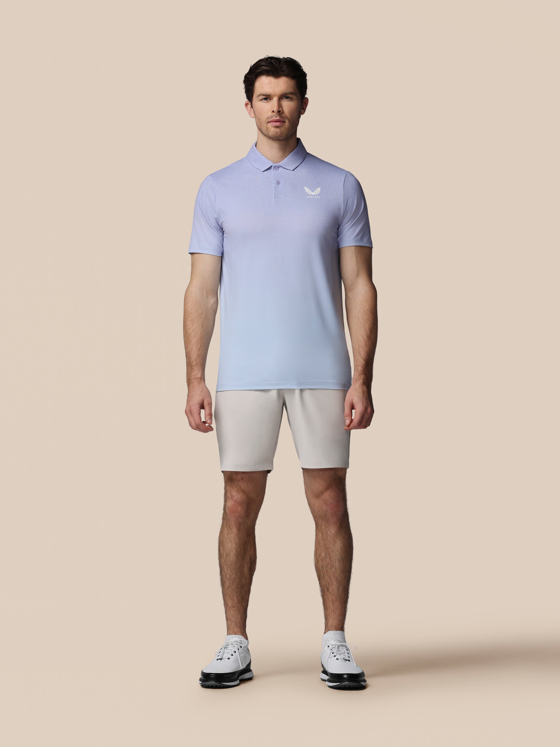 Man wearing a light purple polo shirt and beige shorts on a beige background