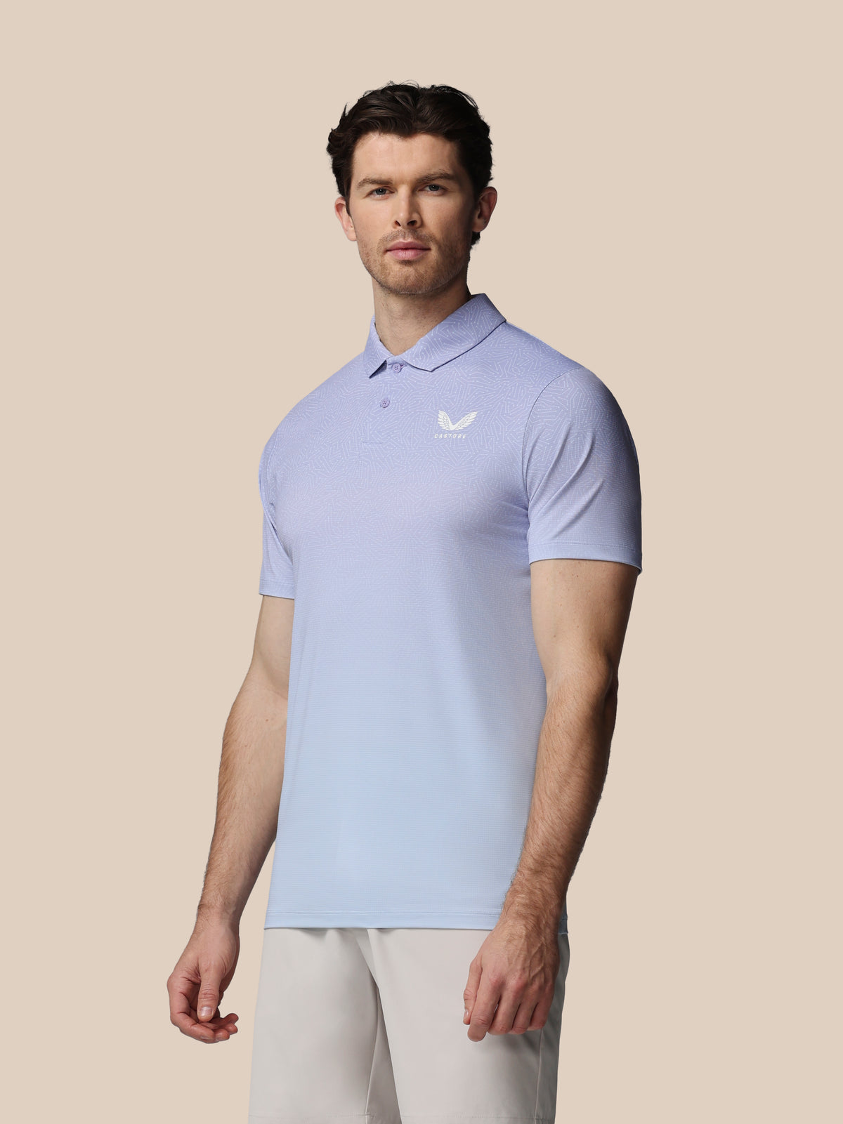 Man wearing a light purple polo shirt with a logo on a beige background