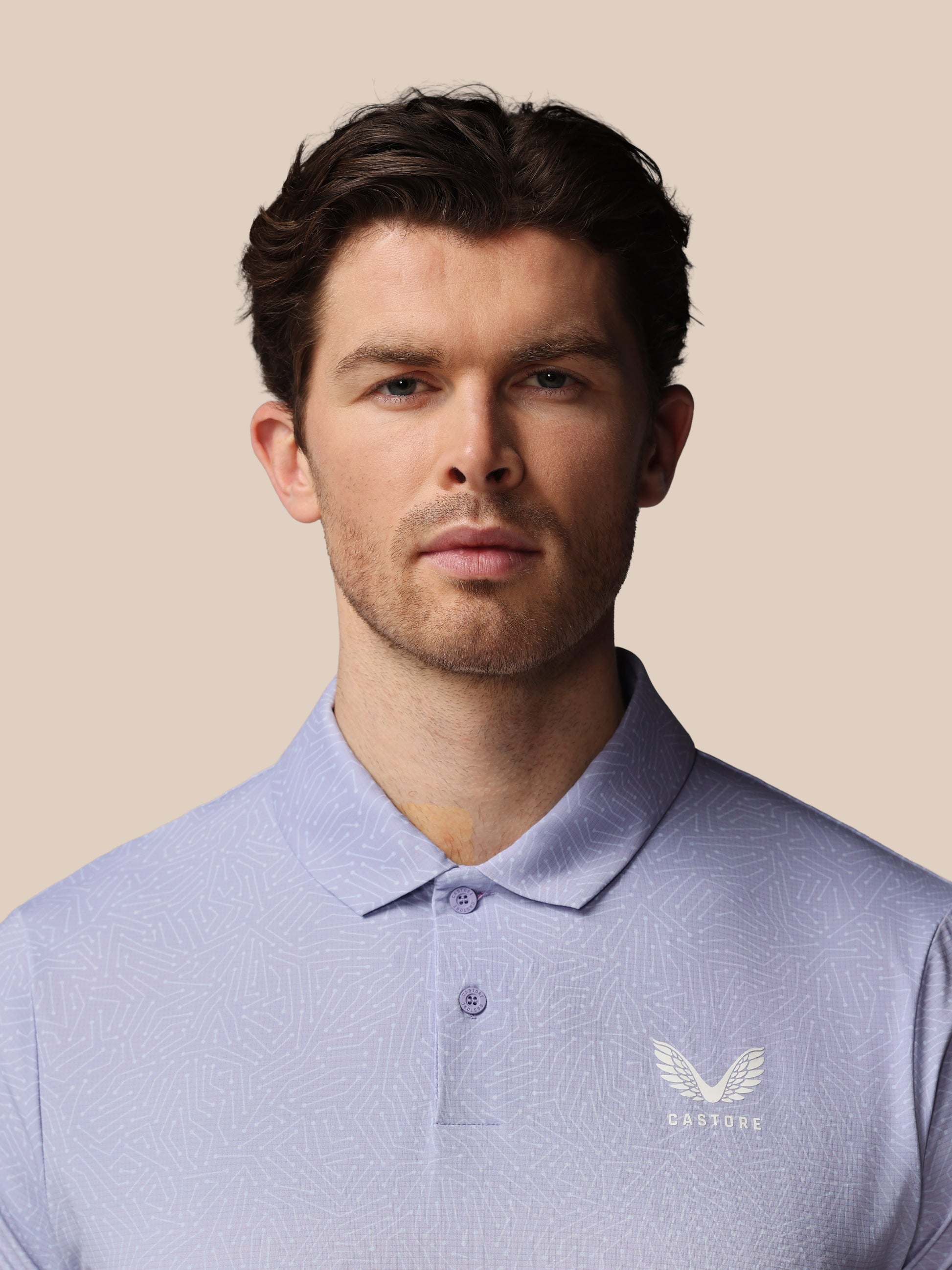 Man wearing a light blue polo shirt with a logo on a beige background