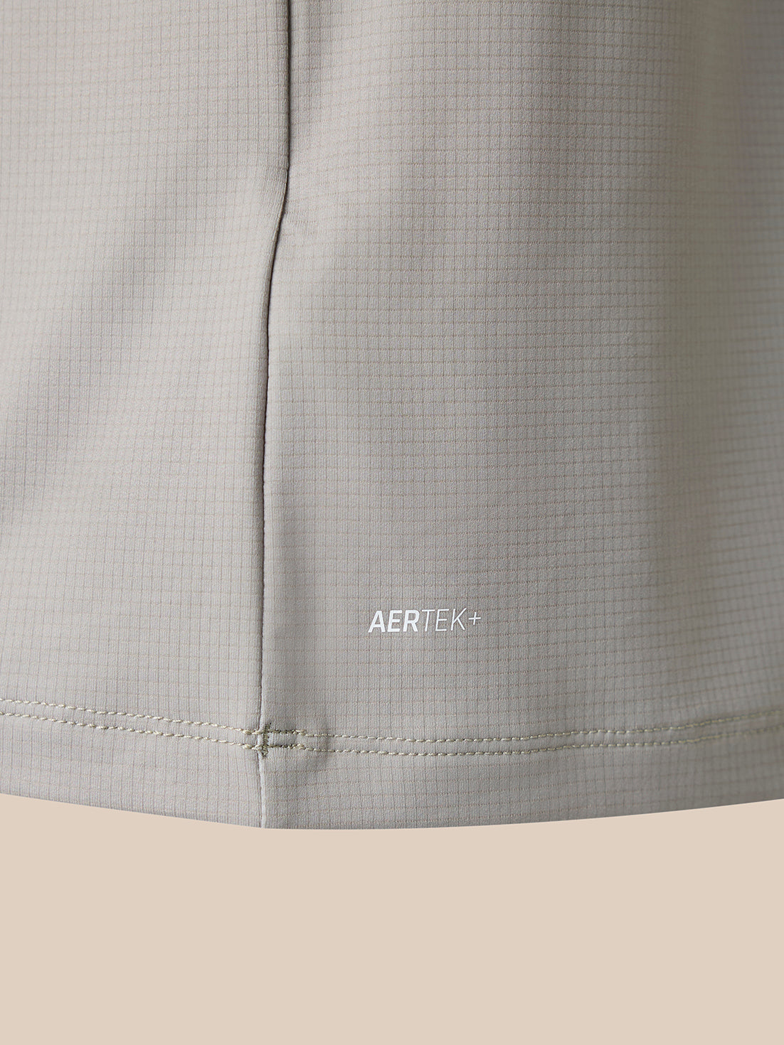 Close-up of a light beige athletic garment showing the AERTEK+ logo and fine grid texture fabric.