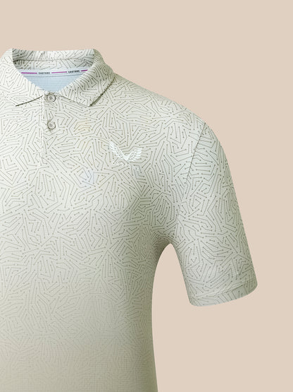 A close-up of a short-sleeve polo shirt with a light beige and white geometric pattern, featuring a small white embroidered eagle logo on the chest. The shirt is shown on a solid beige background.
