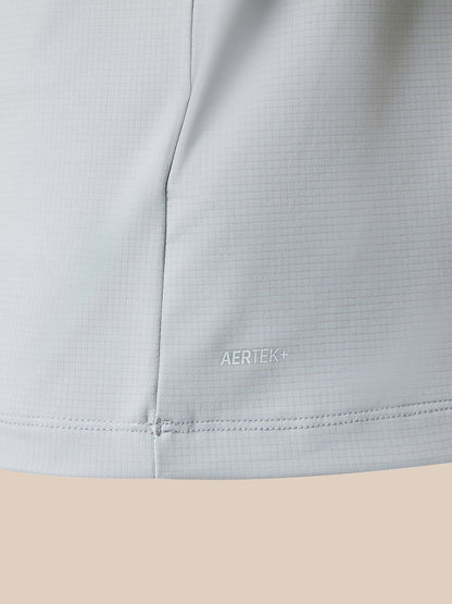 Close-up of a light gray athletic fabric with a fine grid texture, showing a vertical seam and the AERTEK+ logo printed subtly near the lower front. The fabric is shown against a solid beige background.