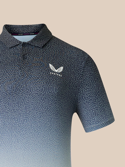 A close-up of a short-sleeve polo shirt with a dark blue and gray geometric pattern, featuring a white embroidered Castore logo on the left chest, set against a solid beige background.