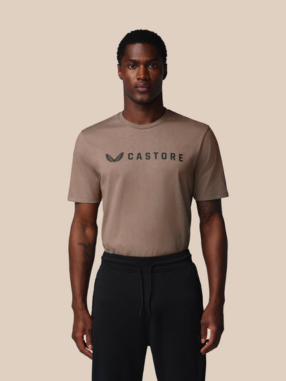 Man wearing a beige t-shirt with 'Castore' logo on a beige background