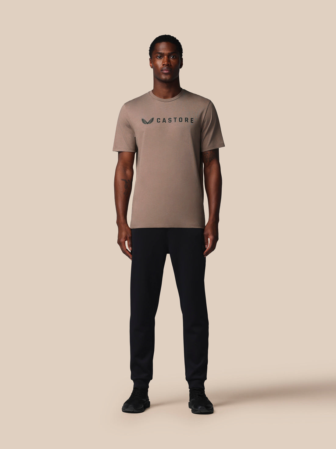 Man wearing a beige t-shirt with a logo on a beige background