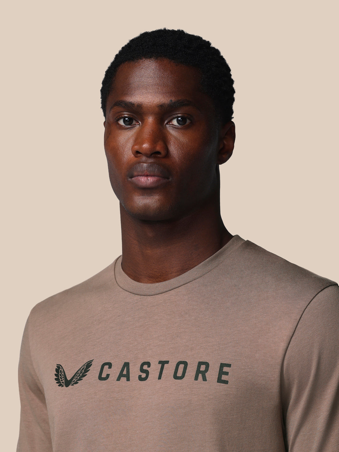 Man wearing a brown t-shirt with 'CASTORE' logo on a beige background