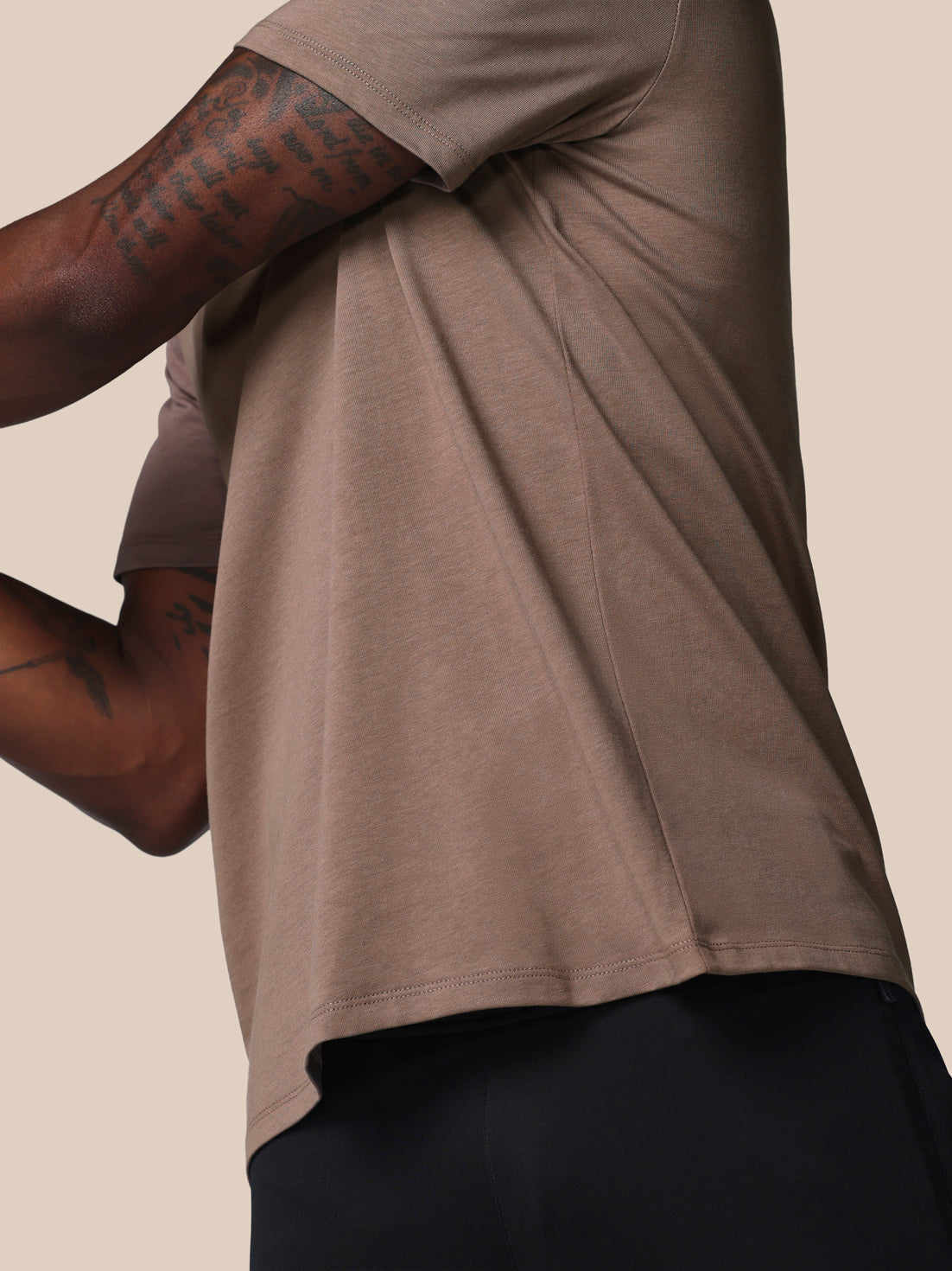 Person wearing a brown t-shirt with rolled-up sleeves on a beige background