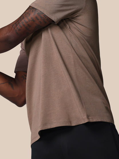 Person wearing a brown t-shirt with rolled-up sleeves on a beige background