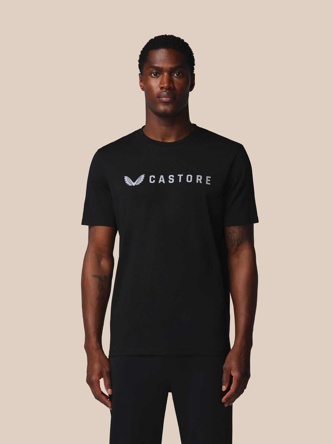 Man wearing a black t-shirt with 'Castore' logo on a beige background
