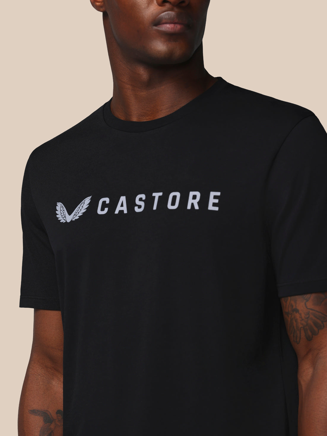 Person wearing a black t-shirt with 'CASTORE' logo on a beige background