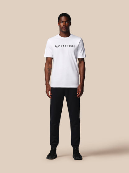 Person wearing a white t-shirt with 'Castore' logo and black pants on a beige background