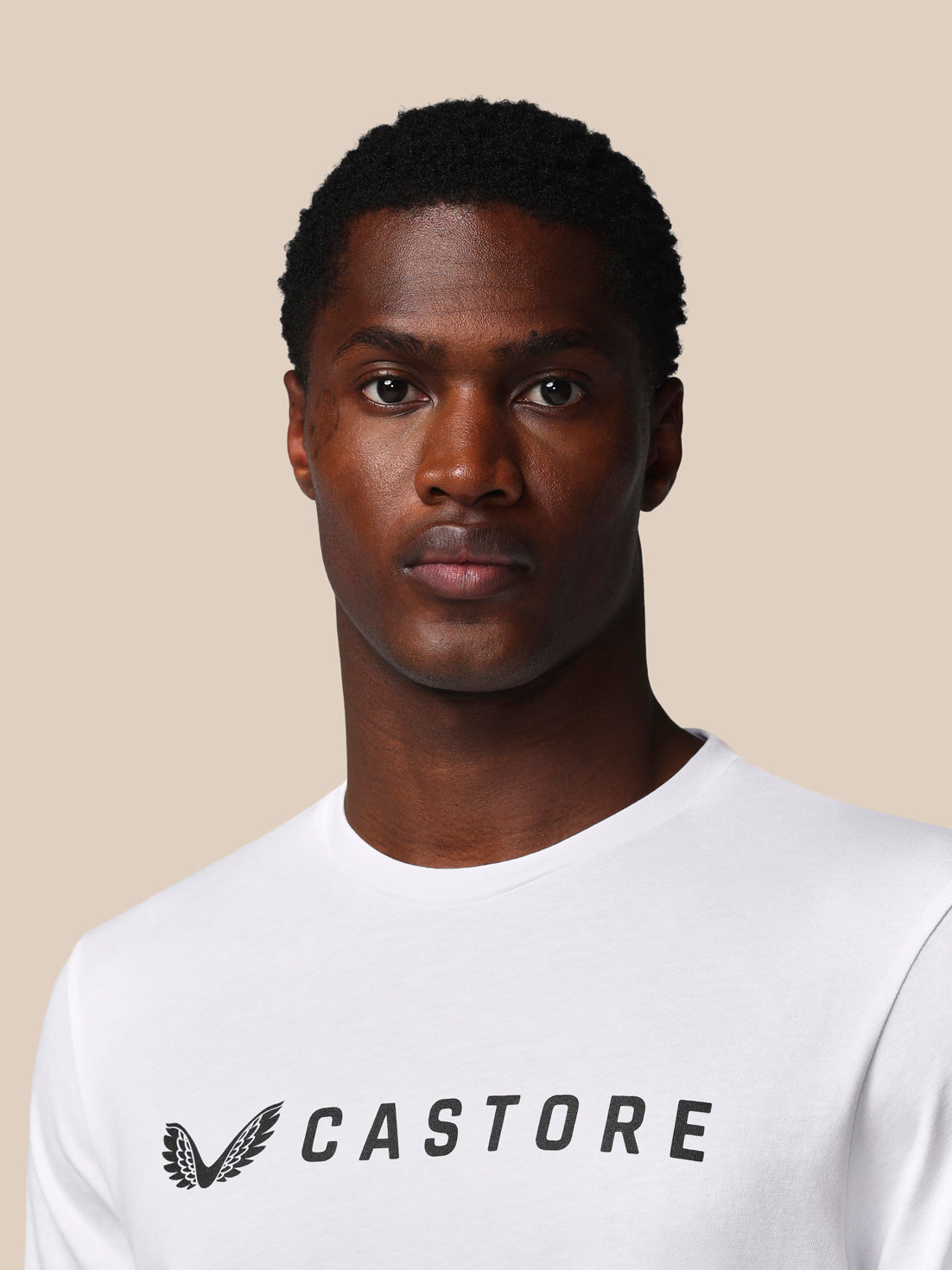 Man wearing a white t-shirt with 'Castore' logo on a beige background