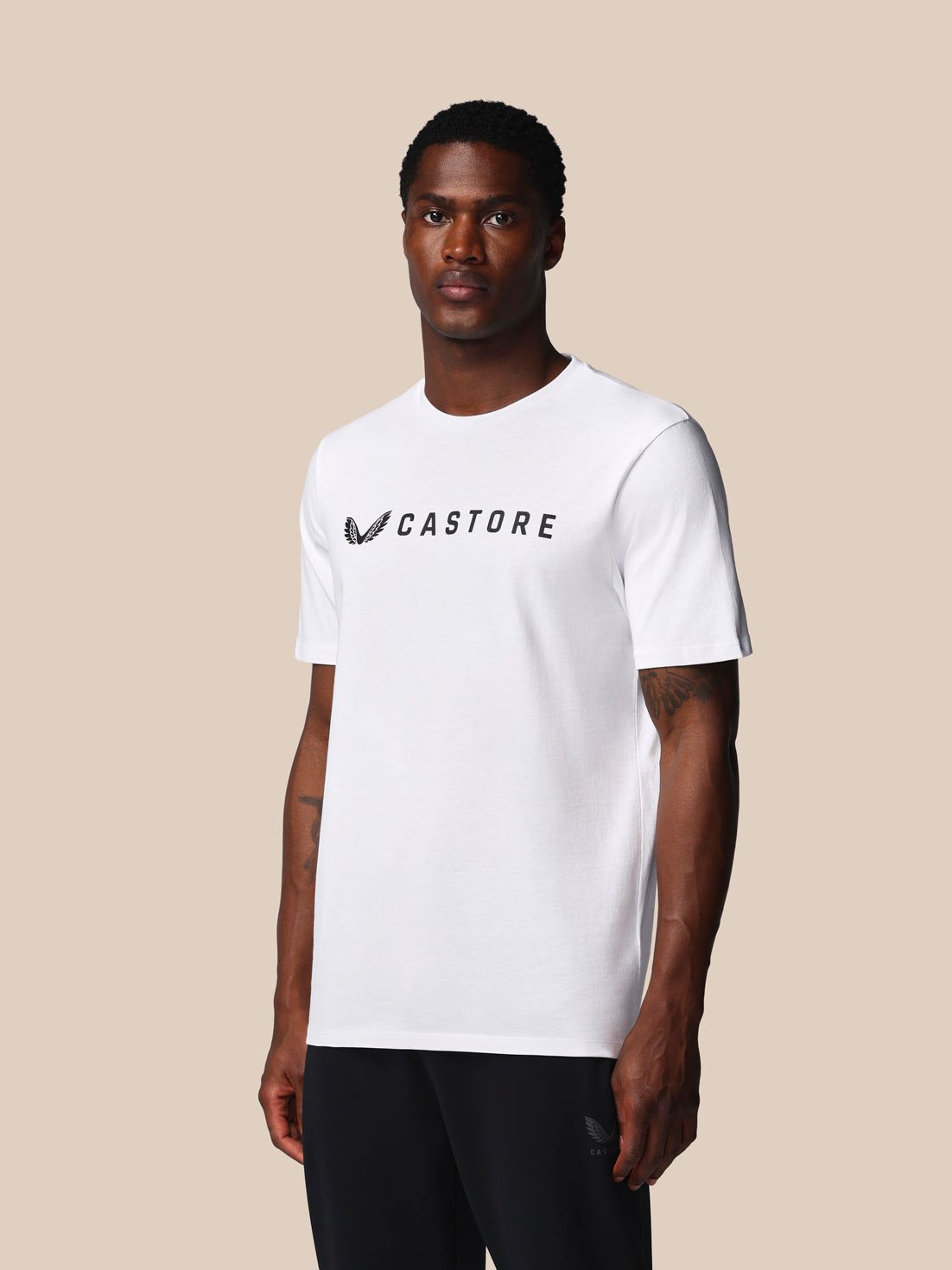 Man wearing a white t-shirt with 'CASTORE' logo on a beige background