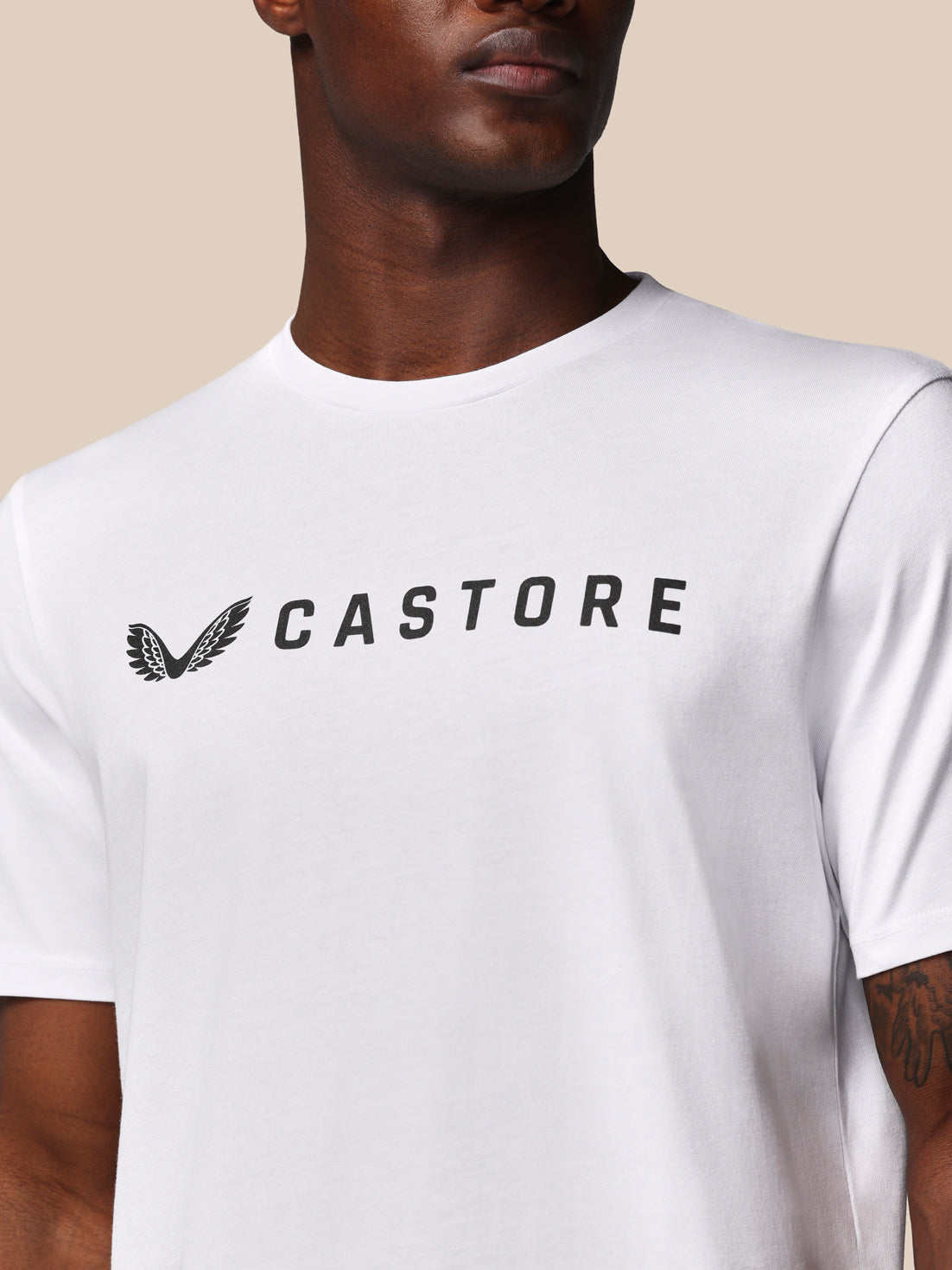 Person wearing a white t-shirt with 'CASTORE' logo on a beige background