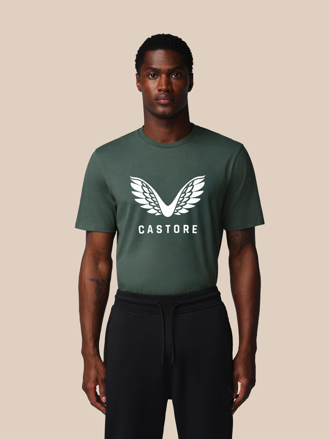 Man wearing a green t-shirt with 'Castore' logo on a beige background