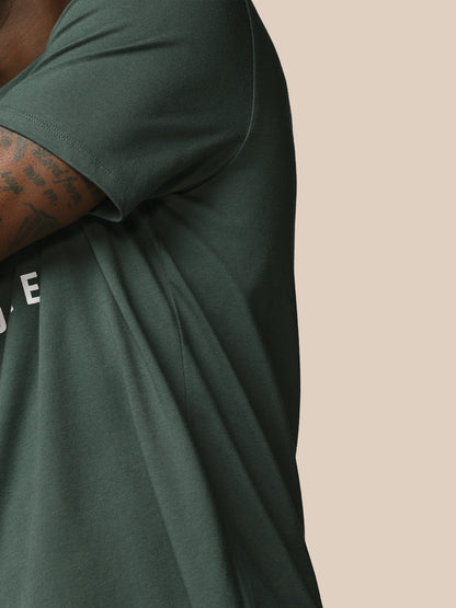 Person wearing a dark green t-shirt with a visible brand logo on a beige background