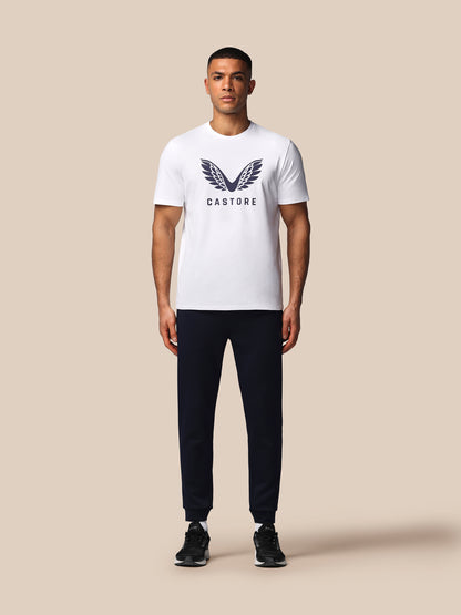 Man wearing a white t-shirt with a logo and black pants on a beige background