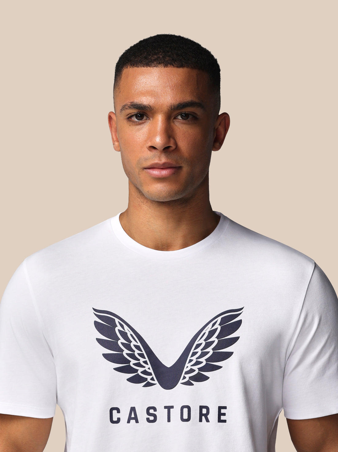 Man wearing a white t-shirt with a logo and 'Castore' text on a beige background