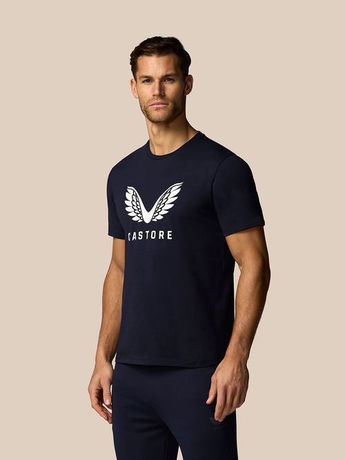 Man wearing a navy blue t-shirt with a logo on a beige background
