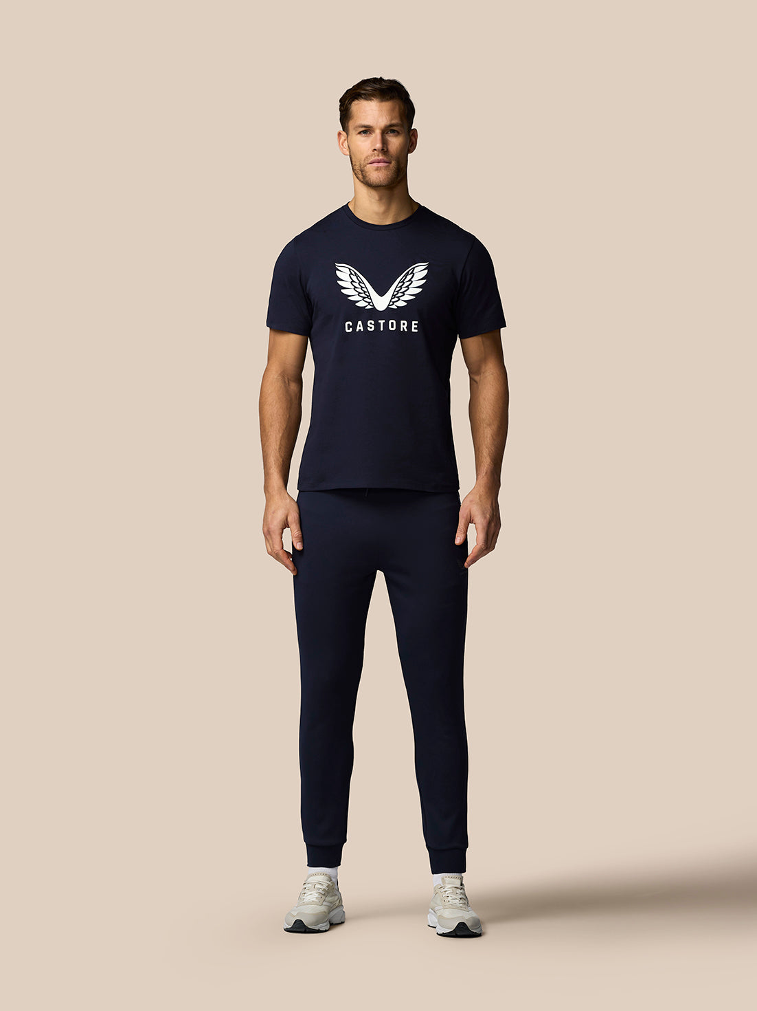 Man wearing navy blue Castore t-shirt and pants on a beige background