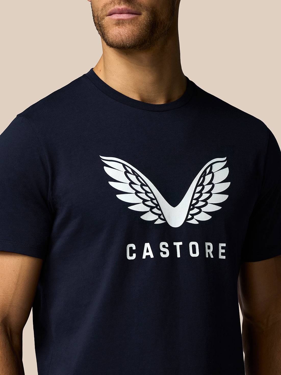 Person wearing a navy blue t-shirt with a white 'Castore' logo on a beige background