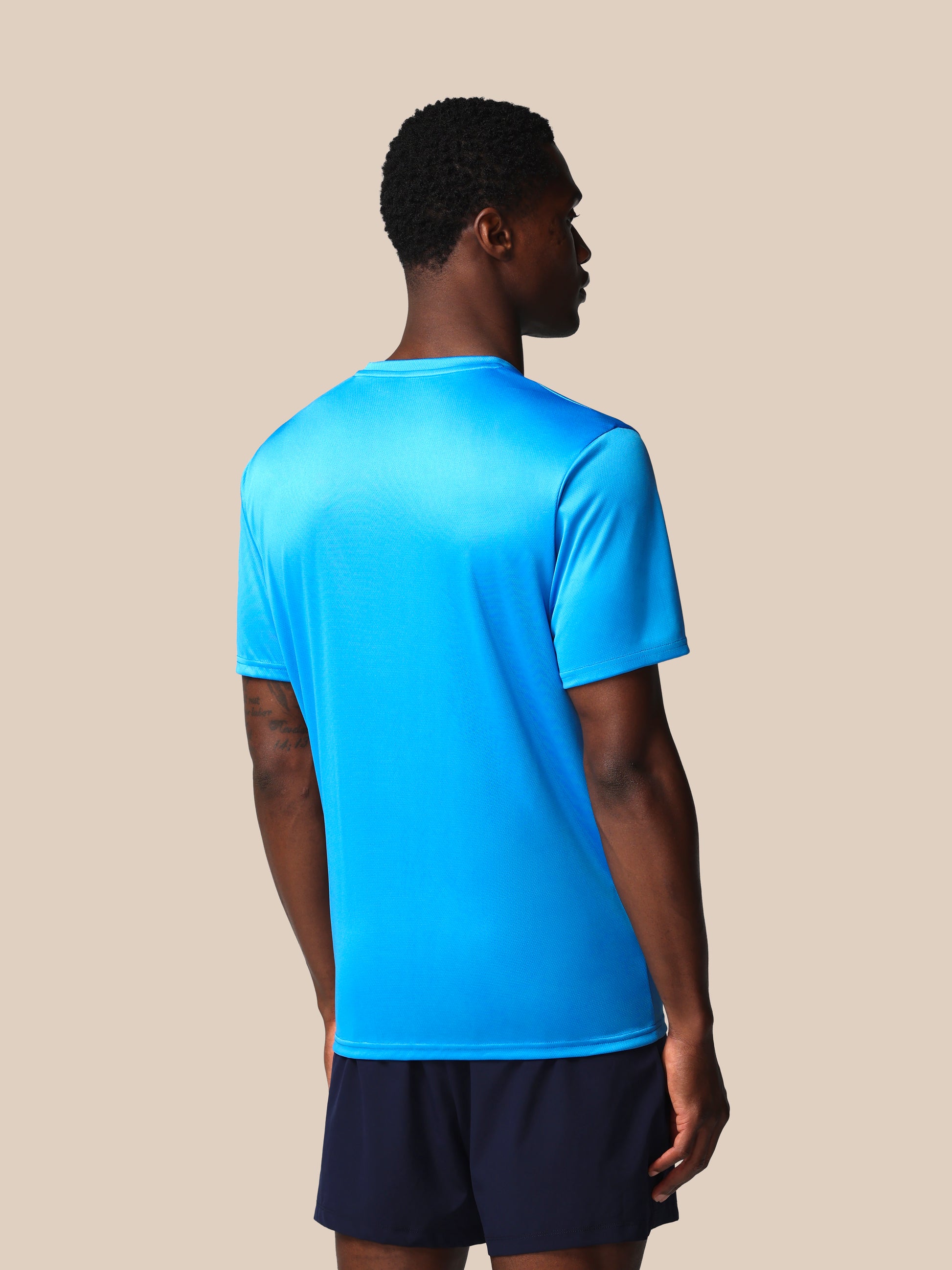 Person wearing a blue athletic shirt and black shorts on a beige background