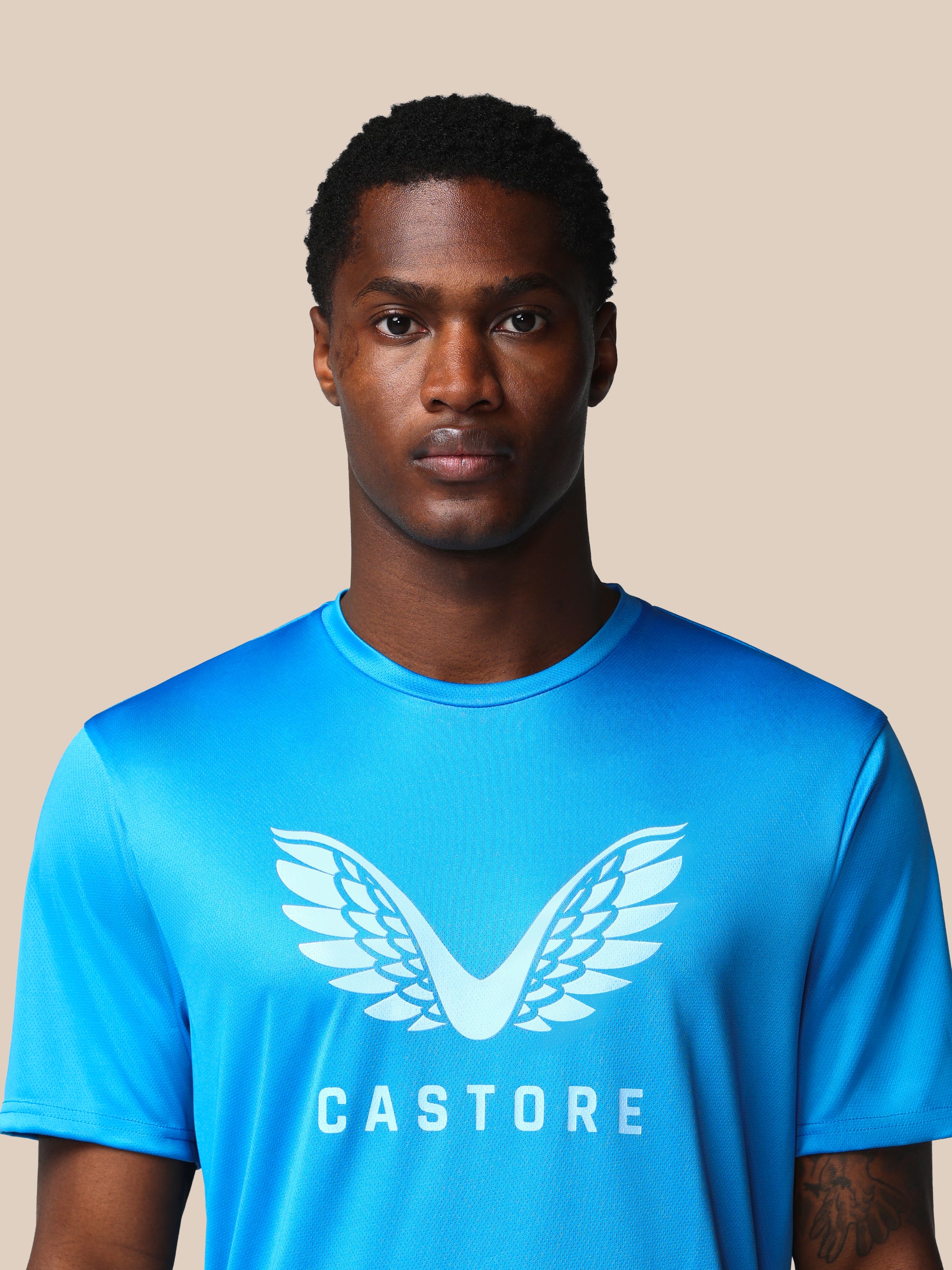 Man wearing a blue Castore t-shirt against a beige background