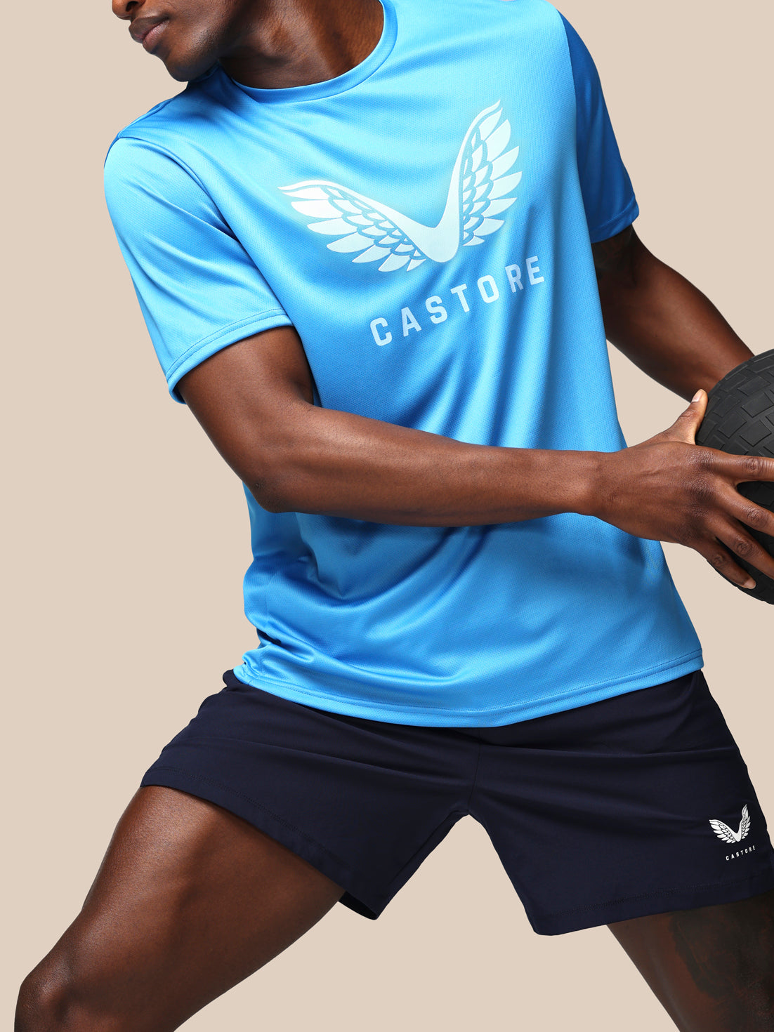 Person wearing a blue Castore sports shirt and black shorts on a beige background