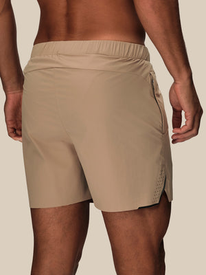 Beige athletic shorts worn by a model, shown from a rear three-quarter view against a solid light beige background.