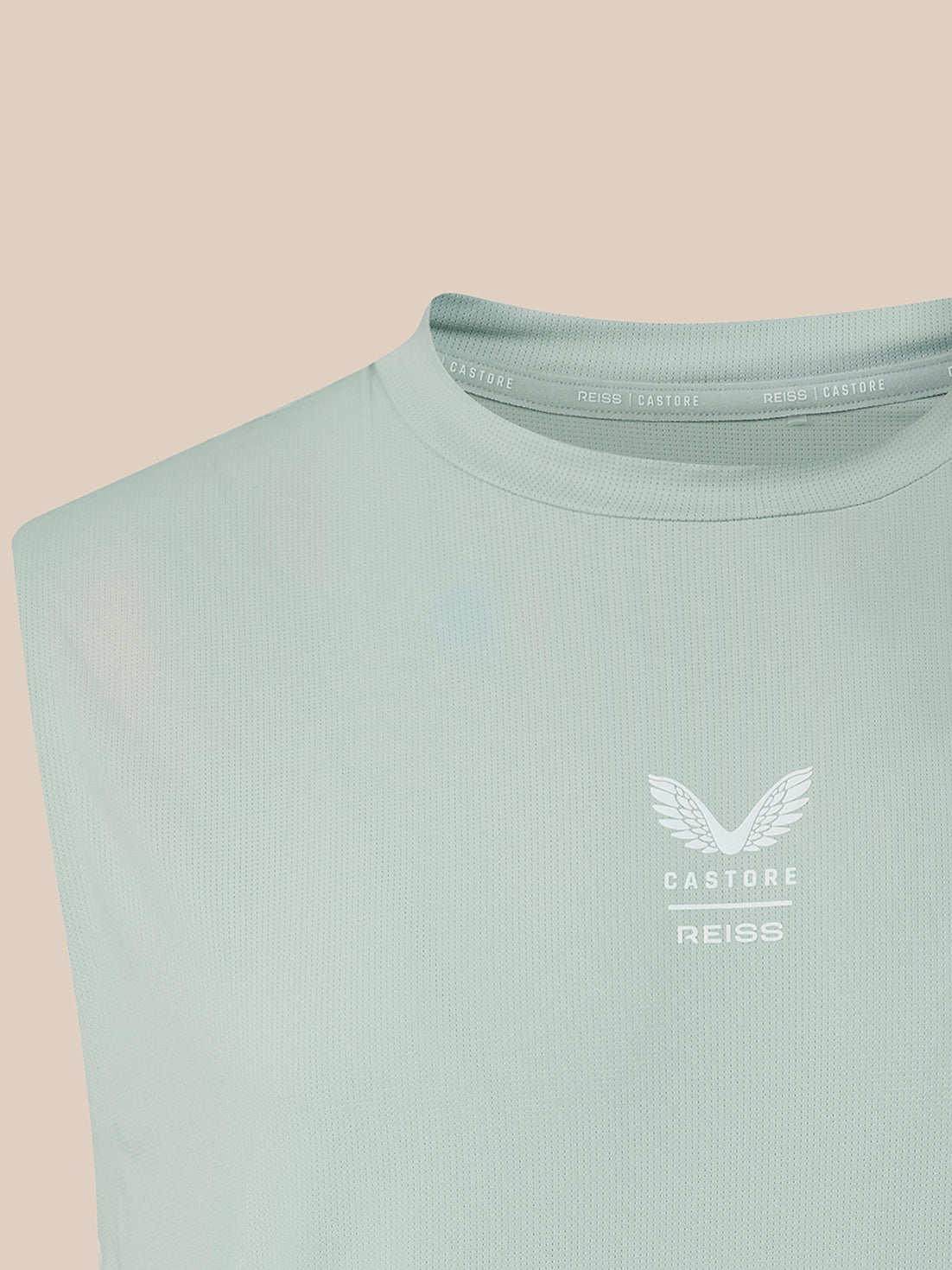 A close-up of a sleeveless ribbed top in a pale mint green color, featuring a white winged logo and the text 'CASTORE REISS' on the left chest, set against a solid beige background.