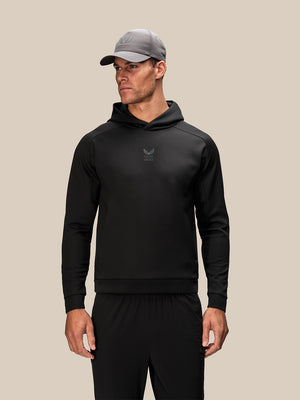 Male model in black Reiss x Castore Flex Hoodie with hood down and a grey cap