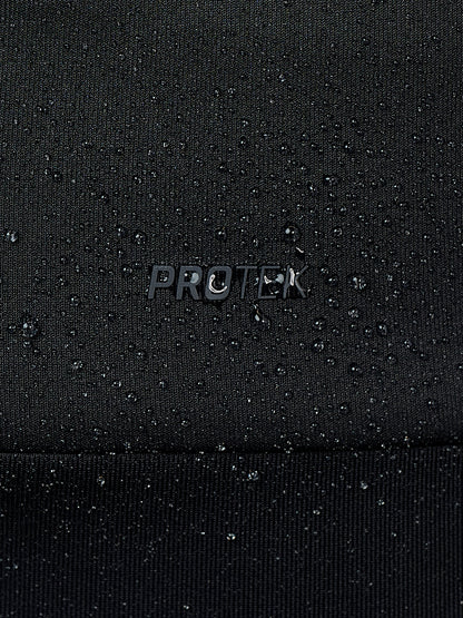 Close-up of a black textured fabric with water droplets beaded on the surface and a small metallic 'PROTEK' logo in the center.