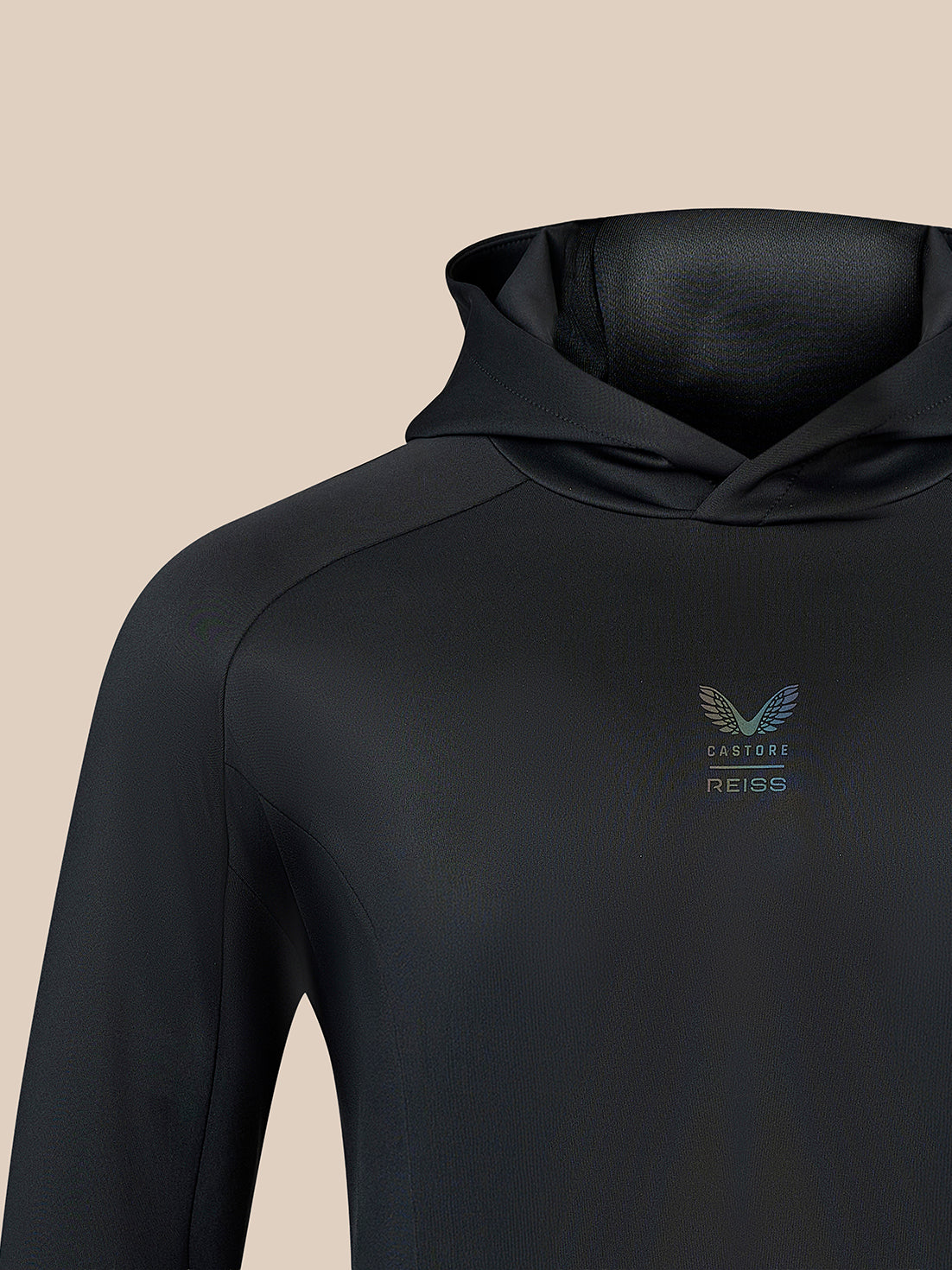 Close-up of a black hooded long-sleeve top with a small winged logo and the text 'CASTORE REISS' on the left chest, shown against a plain beige background.