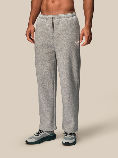 A man wearing light gray heather sweatpants and gray athletic sneakers, shown from the waist down against a plain beige studio background.