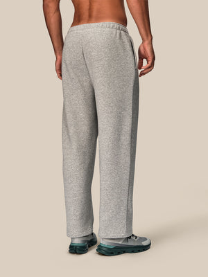 A man shown from the back wearing light heather gray sweatpants and gray athletic shoes, standing against a plain beige studio background.