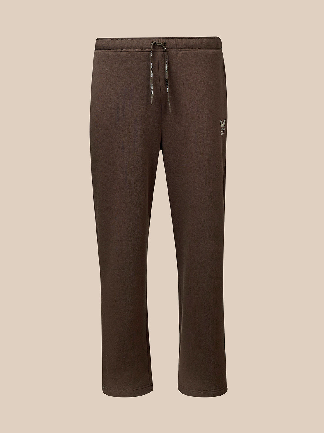 A pair of dark brown sweatpants with a drawstring waist and a small white embroidered logo on the left thigh, shown against a solid beige background.