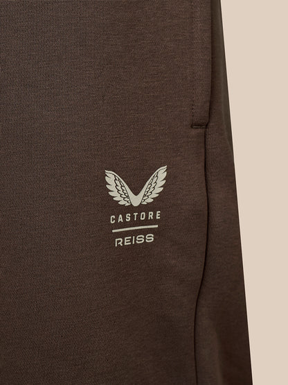 Close-up of a dark brown textured fabric garment featuring a white embroidered wing logo and the text 'CASTORE REISS' on the chest.