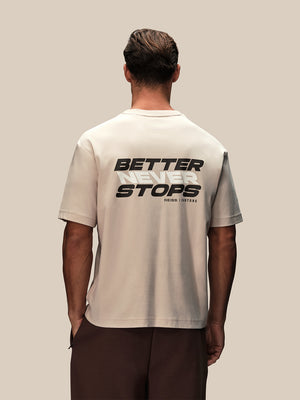 Back view of a man in a stone oversized graphic T shirt with BETTER NEVER STOPS across the back.