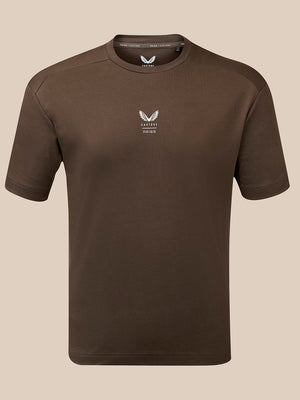 A dark brown short-sleeve crewneck t-shirt with a small white winged logo and 'Castore Reiss' text on the left chest, displayed on a neutral beige background.