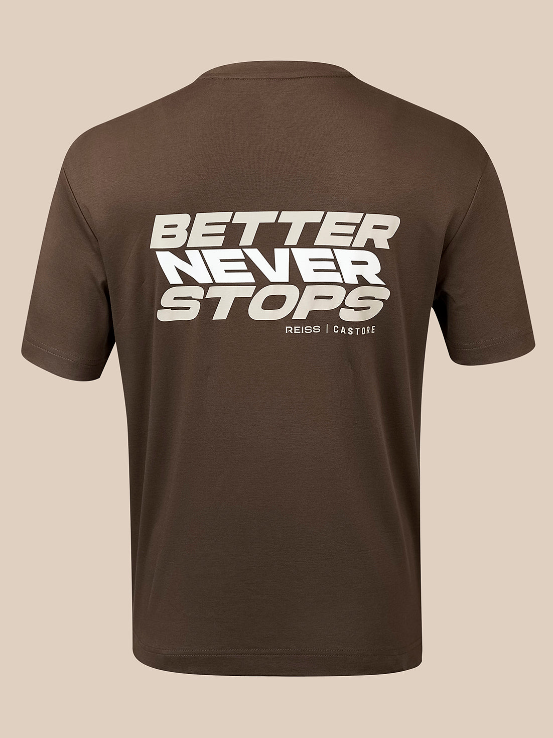 A brown short-sleeve t-shirt shown from the back, featuring a bold white graphic print that reads 'BETTER NEVER STOPS' with 'REISS | CASTORE' printed underneath, set against a solid beige background.
