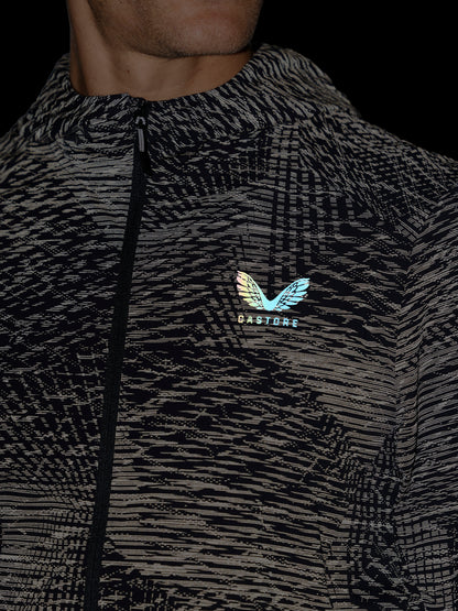 Close-up of a person wearing a black and gray patterned zip-up jacket with a small iridescent wing logo and the word 'CASTORE' on the chest, against a dark background.