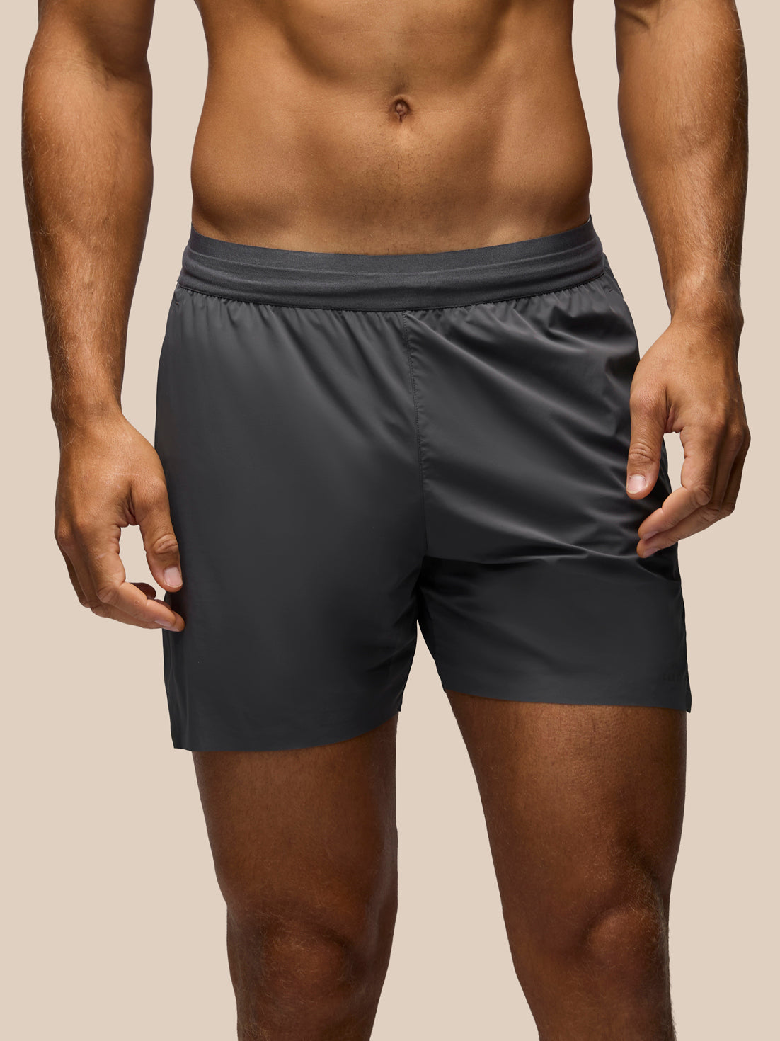 A close-up of a man wearing dark gray athletic shorts, showing the fit from the waist down against a plain beige background.